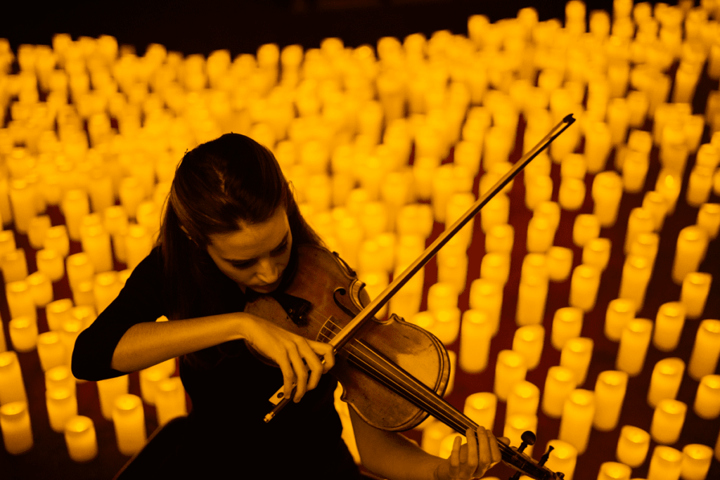 A downward shot of a musician playing the violin with candles in the background