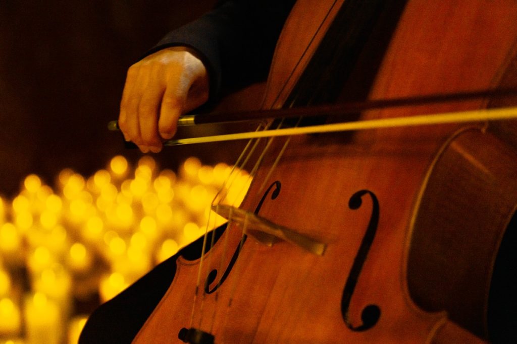 A close up of a musician playing the cello with blurred candles in the background