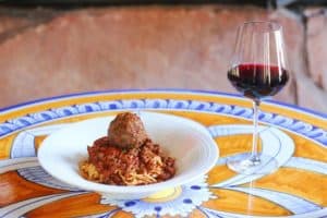 A bowl of pasta and meatballs with a glass of red wine on a tiled table at Grotto Ristorante.