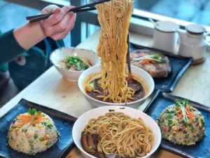 A person holding noodles above a bowl with chopsticks at Shang Artisan Noodle.