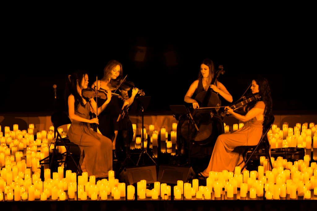 A string quartet performing on a stage covered in hundreds of candles