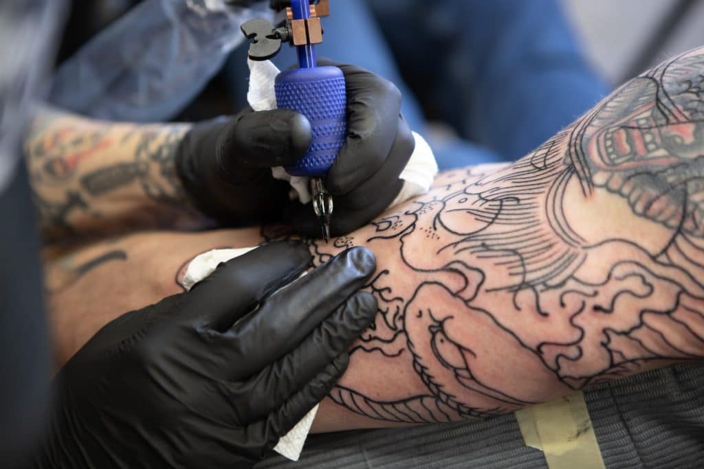A tattoo artist inks a man's arm with a Japanese design.