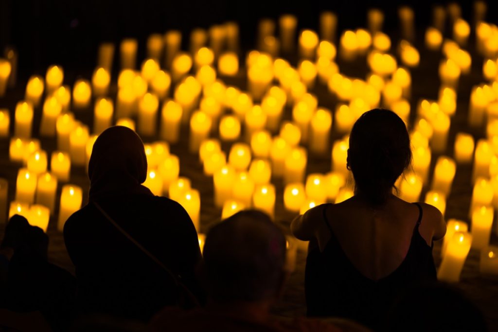 The silhouette of audience members watching a show with countless candles in the background