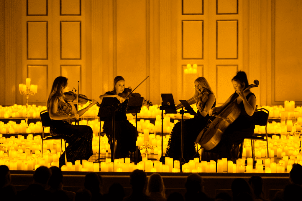A string quartet performing on a raised stage while surrounded by thousands of candles